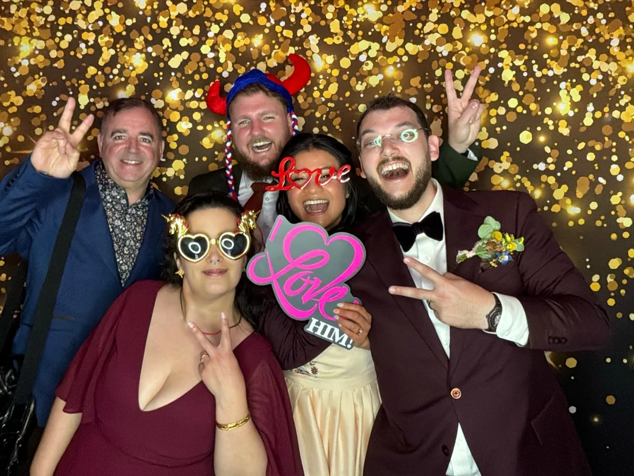 Newlyweds and friends celebrate with wedding props against a gold bokeh backdrop