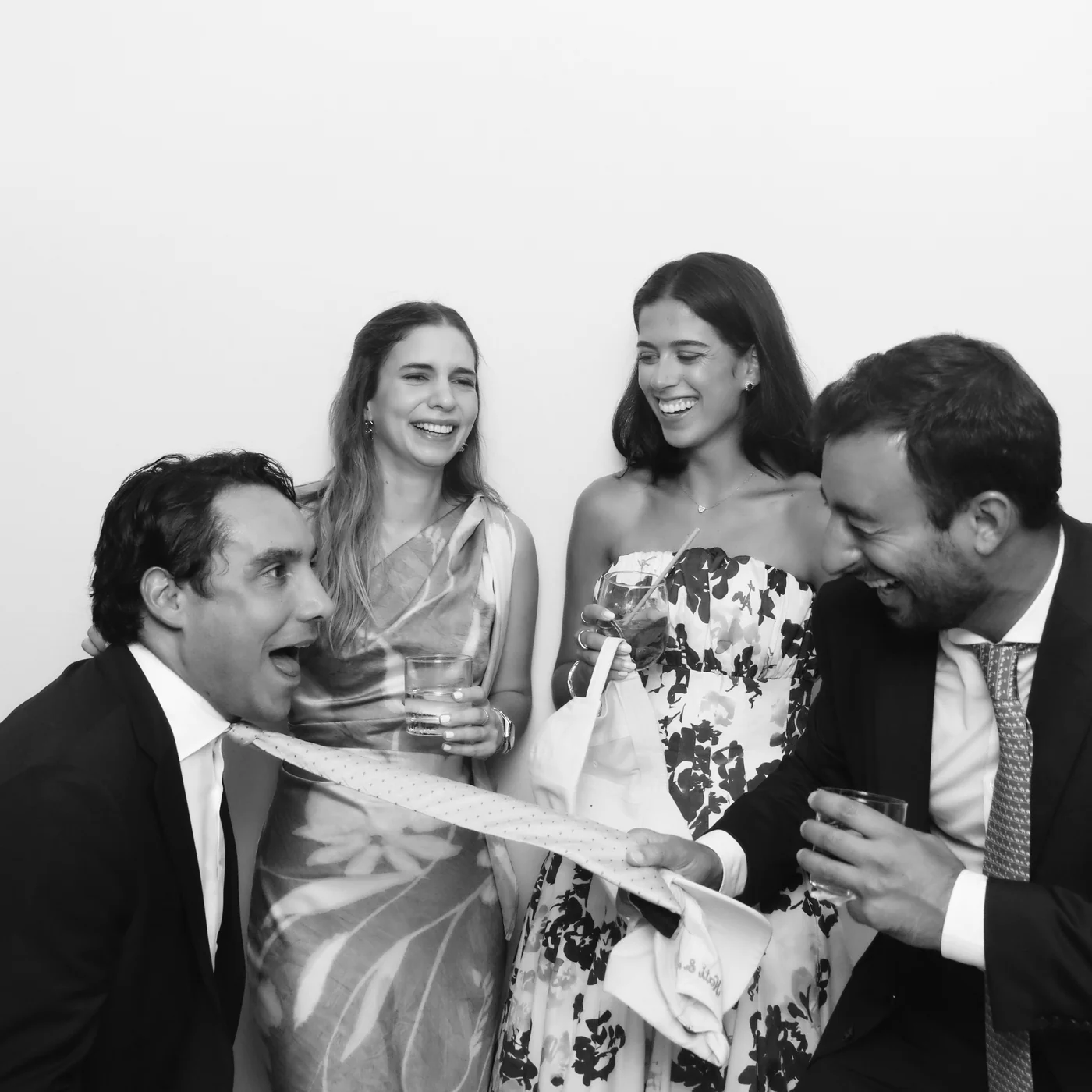 Four wedding guests laughing with a tie prop in a black-and-white Glam photo booth portrait