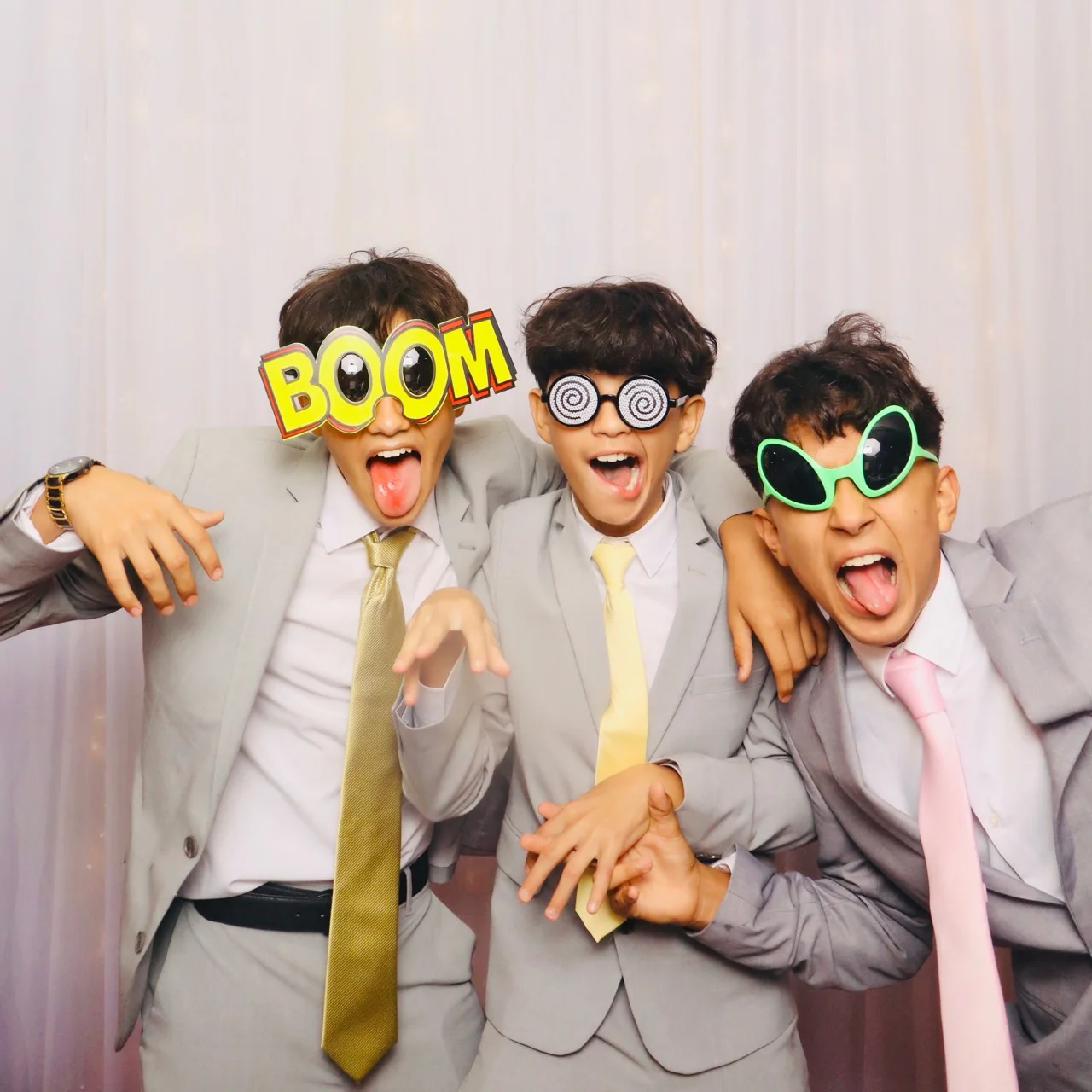 Three quinceañera court members in gray suits wearing oversized novelty glasses