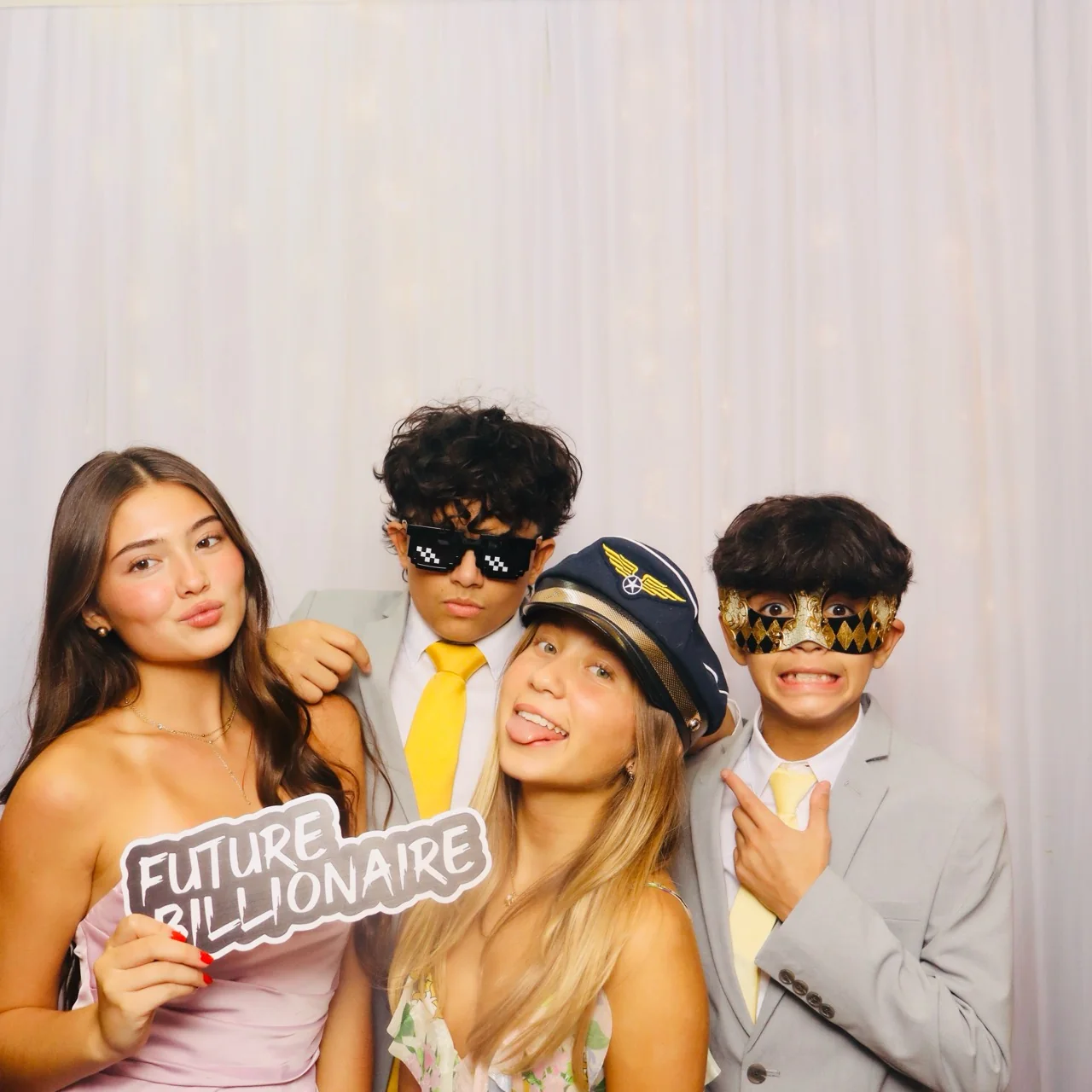 Four quinceañera guests posing with playful glasses, a mask and a Future Billionaire sign