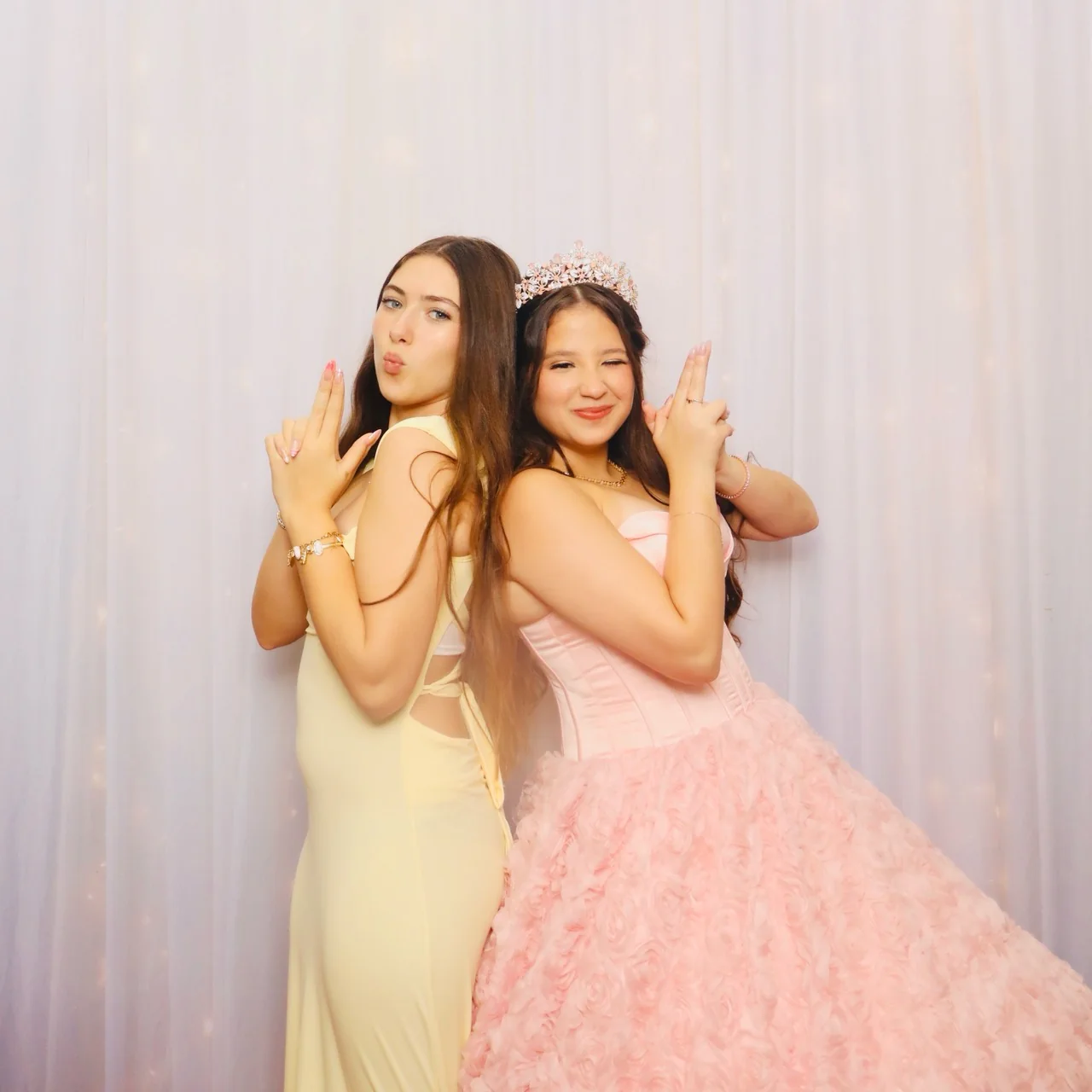 Quinceañera in a pink gown posing back-to-back with a friend in a yellow dress
