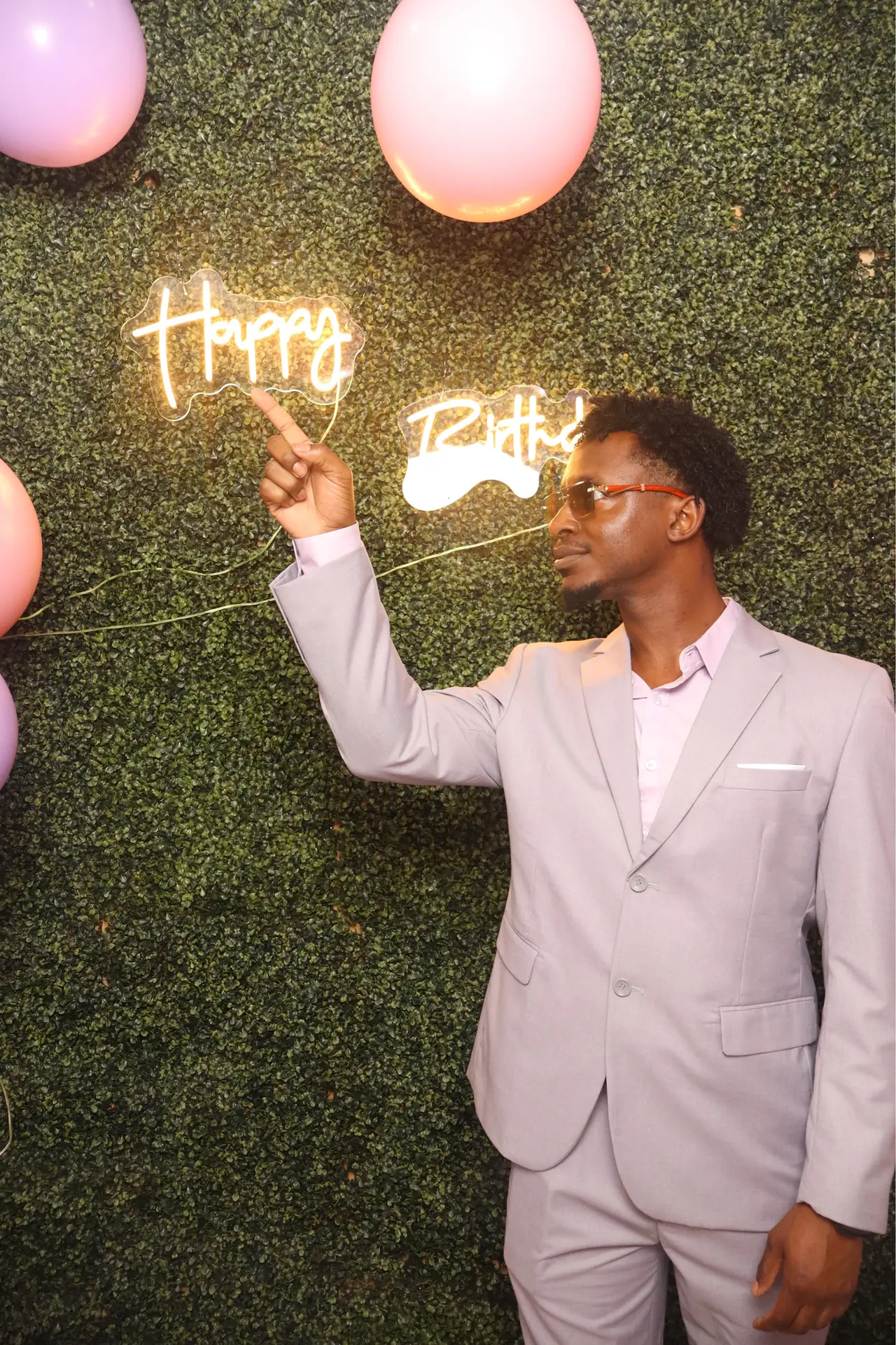 A guest in a lavender suit poses at a birthday photo booth in Sunrise
