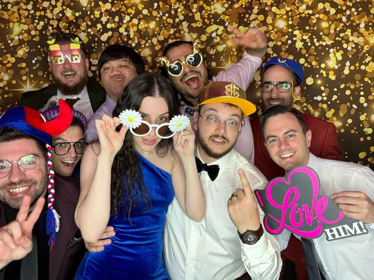Wedding guests crowd together with props in front of a gold bokeh backdrop