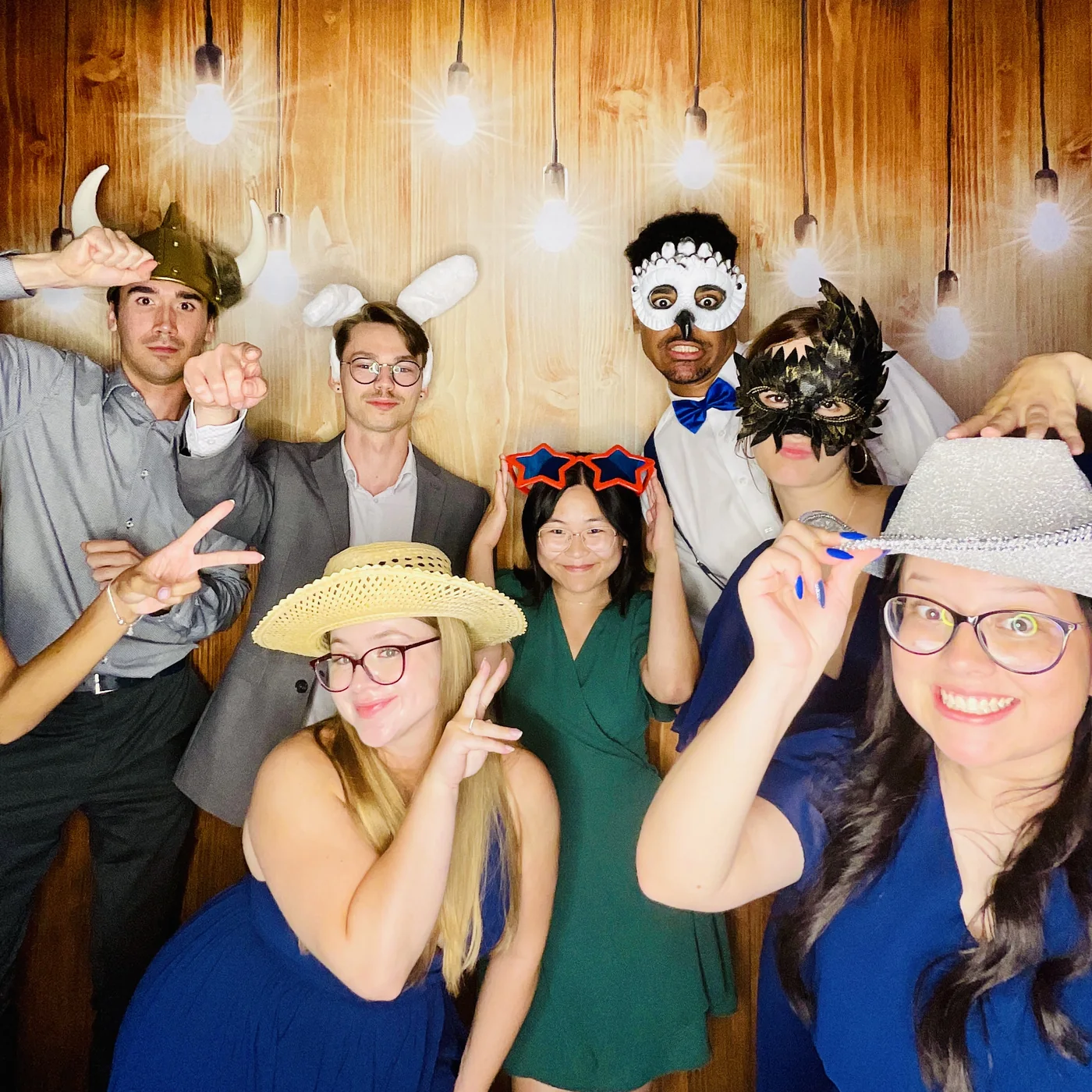 Invitados con máscaras y accesorios en el photobooth con fondo de madera